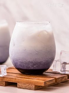 there is a purple and white liquid in a glass on a wooden tray next to some glasses