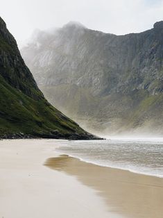 an empty beach with mountains in the background and foggy water on the sand at low tide