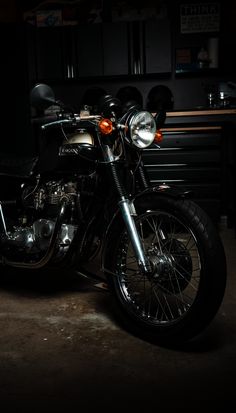 a black motorcycle parked in a garage next to a table and cabinets with lights on it