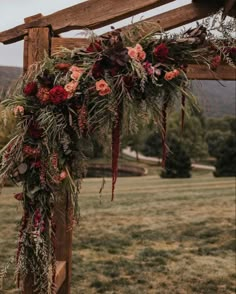 a wooden arch with flowers and greenery hanging from it's sides in the middle of a field