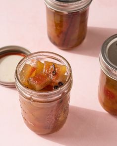 three jars filled with fruit sitting on top of a pink tablecloth next to each other