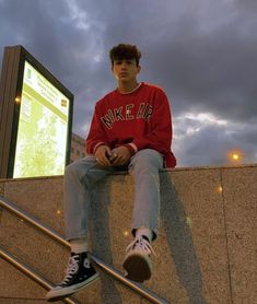 a young man sitting on top of a cement wall next to a metal hand rail