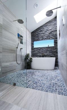 a modern bathroom with stone walls and flooring, along with a skylight above the bathtub