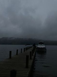 a boat is docked at the end of a pier on a cloudy day with mountains in the distance