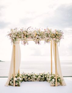 an outdoor ceremony setup with flowers and greenery on the ground, overlooking the ocean