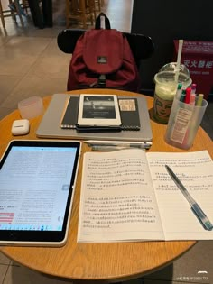 a table with an ipad, notebooks and pen on it in front of a red backpack