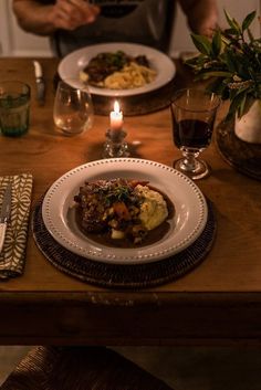 a person sitting at a table with plates of food in front of them and candles on the table