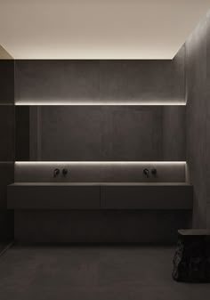 an empty bathroom with two sinks and some lights on the wall above it is lit up by recessed lighting