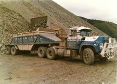 a dump truck is parked in front of a pile of dirt and gravel on the side of a hill