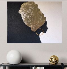 a black and gold art piece on a wall above a book shelf with a white vase