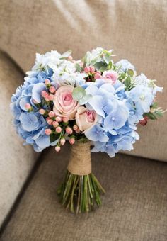 a bouquet of blue and pink flowers sitting on top of a couch next to a pillow