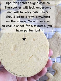 a hand holding a cookie on top of a cooling rack with cookies in the background