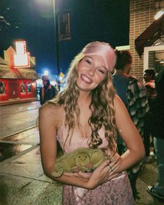 a girl with pink hair holding a teddy bear in her hands and smiling at the camera