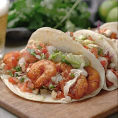 some tacos are sitting on a cutting board next to a glass of beer and lettuce