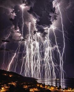 lightning strikes in the sky over water and land at night with buildings lit up by lights