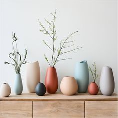 several different colored vases sitting on top of a wooden table next to each other