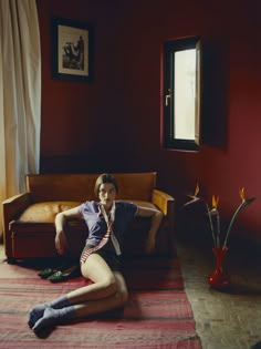 a woman sitting on the floor in front of a couch with her legs spread out