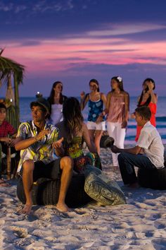 a group of people sitting on top of a sandy beach next to the ocean at sunset