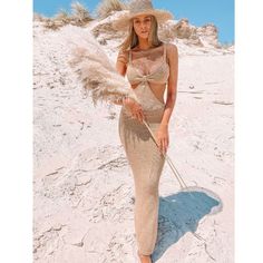 a woman standing on top of a sandy beach wearing a straw hat and long dress