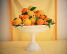 a white bowl filled with lots of oranges on top of a yellow table cloth