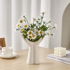 a vase filled with white daisies on top of a table next to a cup and saucer