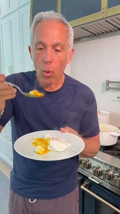 an older man eating food from a white plate in the middle of a kitchen with blue cabinets