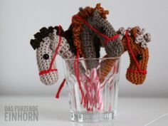 three crocheted horses in a glass with red string tied around their necks and head