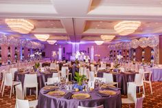 a banquet room set up with purple linens and round tables, white chairs, and chandeliers