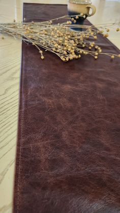 a brown leather table runner with dried flowers on it