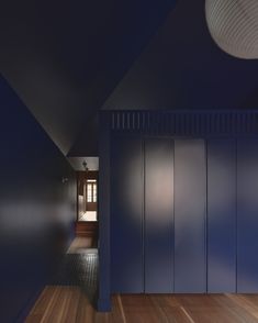 an empty hallway with blue walls and wooden floors is lit by a light that hangs from the ceiling