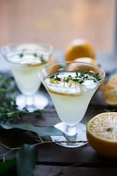 two glasses filled with white wine and garnished with herbs, surrounded by sliced oranges