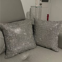 two silver sequin pillows sitting on top of a couch next to a glass vase