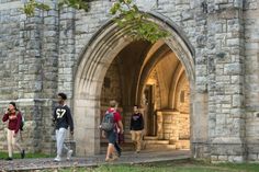 several people are walking in front of an old stone building with arches and doorways