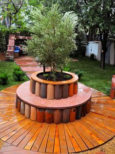 a small tree is growing in the middle of a circular planter on a wooden deck