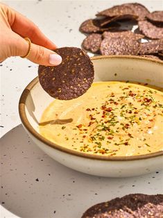 a hand dipping a cracker into a bowl of dip with tortilla chips