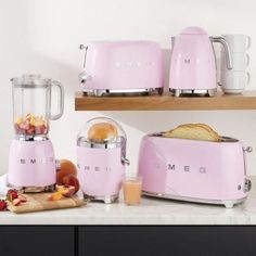 a pink blender sitting on top of a counter next to toasters and fruit