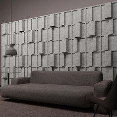 a gray couch sitting in front of a wall covered in cubed tiles and a lamp