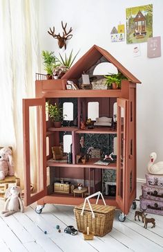 a wooden doll house sitting on top of a floor next to stuffed animals and toys