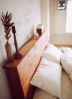 a bed with white sheets and pillows next to a small plant on the headboard