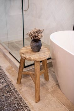 a potted plant sitting on top of a wooden stool next to a bath tub