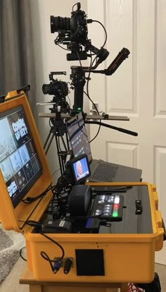 a laptop computer sitting on top of a yellow box next to a camera set up in front of a door