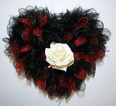 a white rose sitting on top of a black and red heart shaped wall hanging decoration