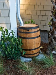 a wooden barrel sitting in front of a house next to some bushes and plants on the ground