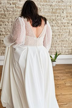 a woman standing in front of a brick wall wearing a white dress with long sleeves