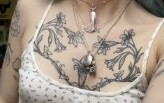 a woman with tattoos on her chest wearing a white tank top and silver necklaces