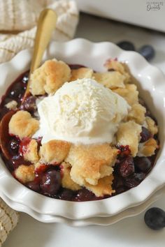 a bowl filled with fruit and ice cream on top of a white plate next to blueberries