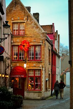 two people walking down the street in front of some buildings with red doors and windows