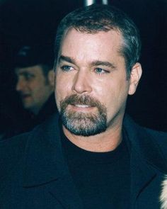 a close up of a person wearing a black shirt and coat with a goatee