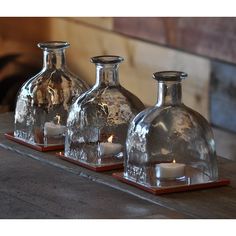 three glass vases sitting on top of a wooden table next to a candle holder