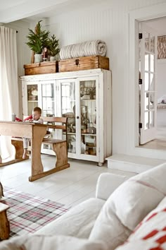 a small child sitting at a table in front of a white cabinet with glass doors